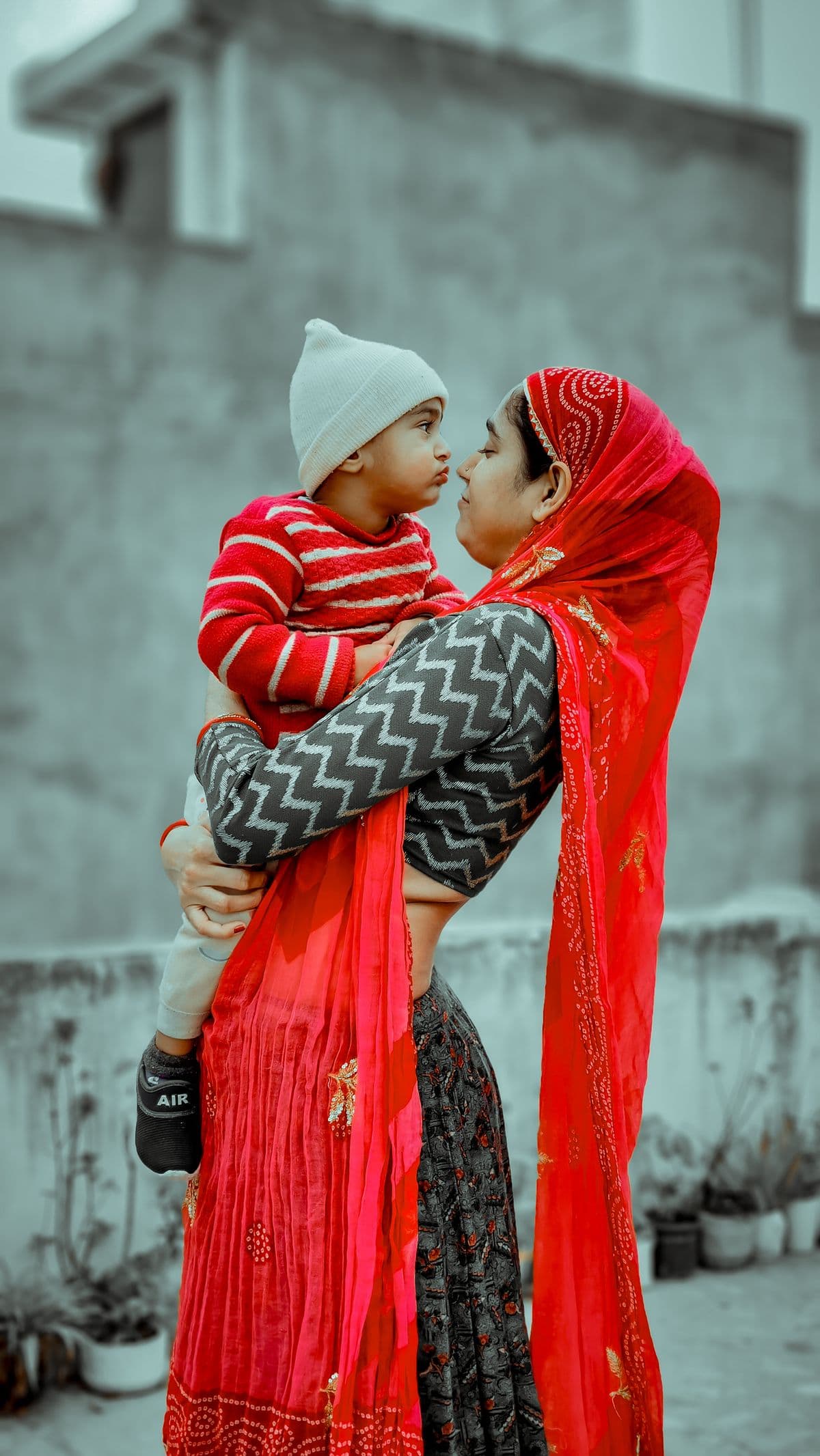 A Pakistani mother in a red dupatta holding her little son nose-to-nose on a rooftop