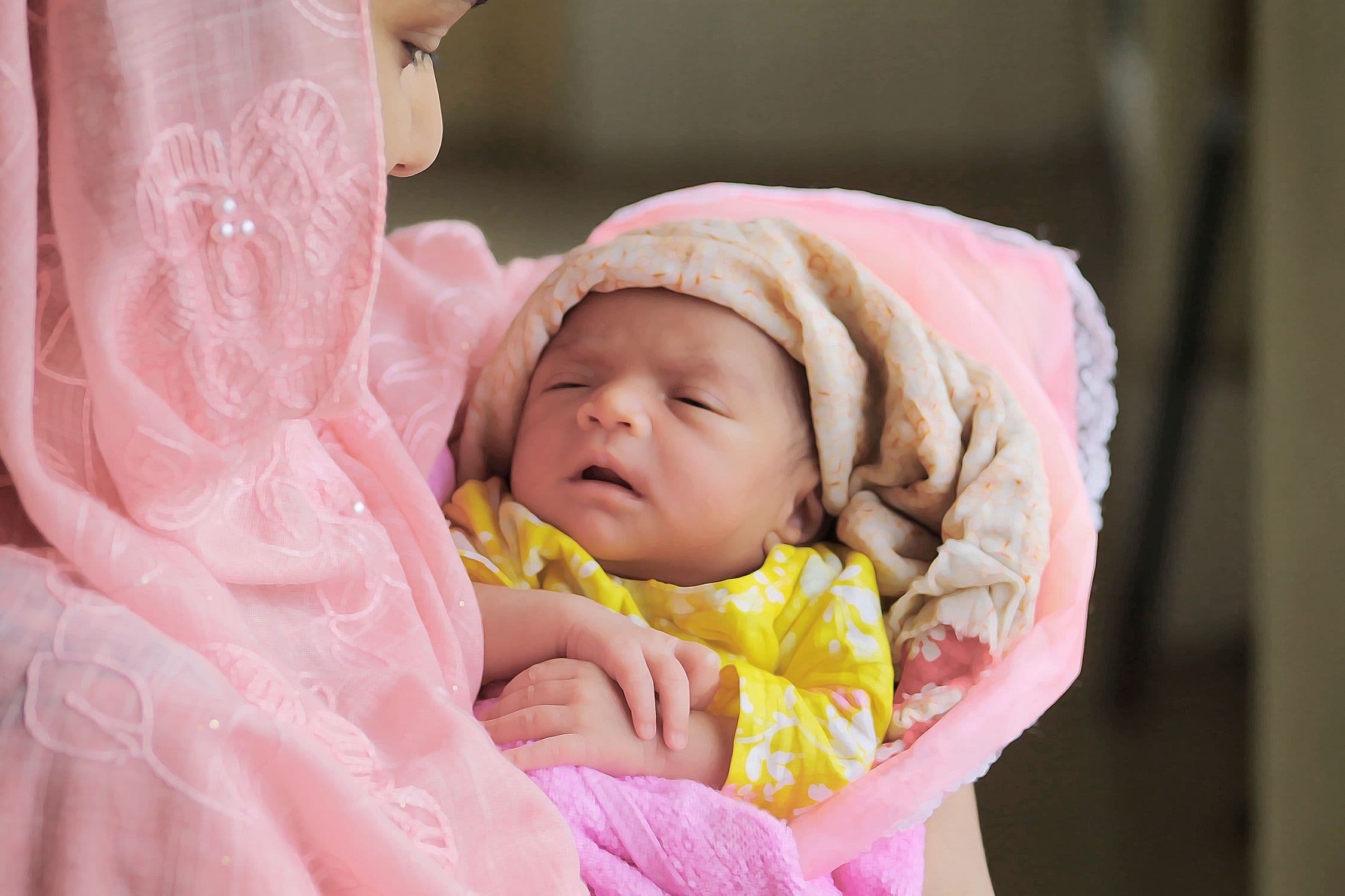 A South Asian mother in a pink dupatta cradling her sleeping newborn