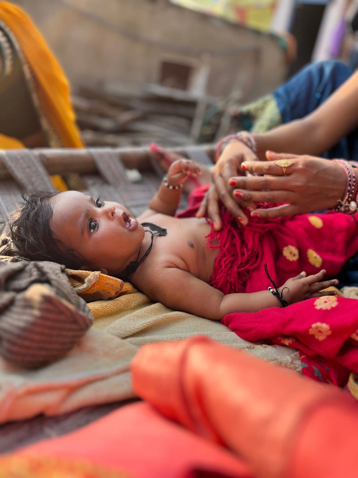 A South Asian baby on a traditional charpai with mother's hands gently caring for them